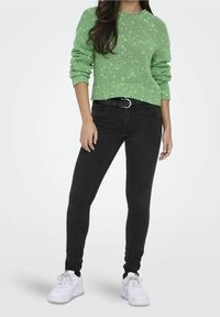 Zielony dziergany sweter z fakturowanym wzorem, połączony z czarnymi jeansami o dopasowanym kroju i białymi trampkami. Posiada pasek z okrągłą klamrą.