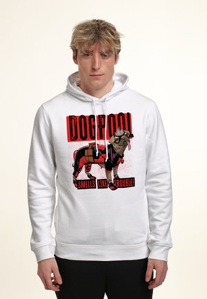 Young man wearing white hoodie with graphic of dog dressed as Deadpool and text "DOGPOOL smells like trouble" on front.