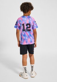 Kortärmad, gradient lila-rosa tröja med svart "12" och detaljer; i kombination med svarta shorts. Vita strumpor med svart chevronmönster.