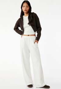 Bruine cropped zip-up hoodie over een witte fitted T-shirt en losse witte sweatpants met zijzakken, met een casual, ontspannen pasvorm.