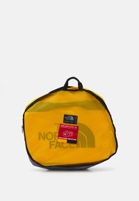 Yellow mesh duffel bag with a black bottom, featuring "THE NORTH FACE" logo and tag labeled "BASE CAMP DUFFEL XXL" on the front.