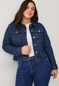 Chaqueta de mezclilla azul oscura con dos bolsillos en el pecho, botones frontales y mangas largas. La tela tiene una textura suave y un ligero desgastado.