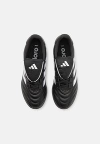 Sorte fotballsko med en teksturert læroverdel, som har tre hvite striper, en rund tå og svarte lisser. Innendørsdesign.
