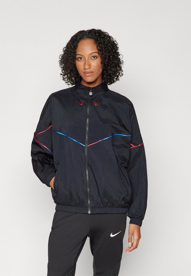 Schwarze Windjacke mit Stehkragen, mit bunten diagonalen Streifen in Rot und Blau, elastischen Bündchen und einem Reißverschluss auf der Vorderseite.