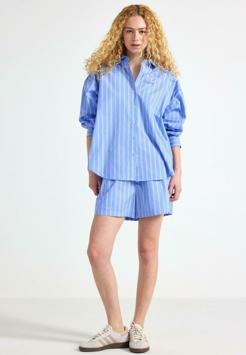 Blå og hvidstribet skjorte og matchende shorts sæt, lavet af let stof. Skjorten har en afslappet pasform og knaplukning foran.