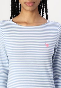 Lyseblå og hvit stripet langermet skjorte laget av mykt stoff, med en liten rosa hjerte-detalj på venstre bryst.