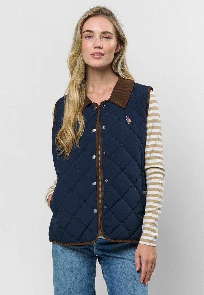 Námornícky prešívaný vest s hnedým kordurovým golierom, cvokovými gombíkmi a vyšívaným logom. Dobre sa kombinuje s pruhovanou dlhoprstou košeľou pod ním.