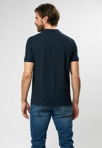 Marineblå polo med korte ærmer, krave og lige kant, parret med lyseblå jeans med baglommers.