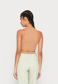 Top cropped canela com nervuras, com um decote redondo e design de costas nadador, combinado com calças altas de cor verde claro, exibindo uma textura suave.