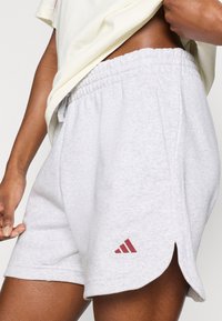 Sive kratke športne hlače z teksturirano površino, elastičnim pasom in stranskimi razporki. Na spodnjem levem boku je bordo adidasov logotip.