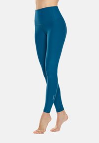 Teal színű, magas derekú leggings, rugalmas anyagból készült, lapos varrásokkal és diszkrét logóval a bokánál. Puha, sima tapintású.