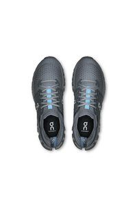 Chaussures de course en maille grises avec des accents bleus, semelle amortissante, bout arrondi et système de laçage. Logo visible sur le côté et sur la semelle intérieure.