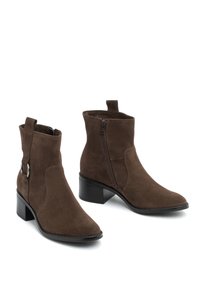 Ruskisat värjatud nahasta pruunid ankle boots, millel on terav nina, külgvahe ja must plokk-kann. Vasakul saapil on dekoratiivne hõbedane aksessuaar.