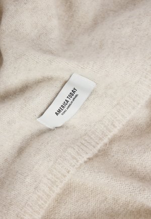 Soft beige knit fabric with a white clothing label sewn on, displaying "AMERICA TODAY ICONIC AMERICAN APPAREL" text.