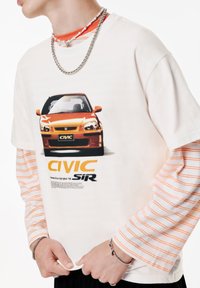 Hvid grafisk t-shirt med orange Honda Civic SIR tryk, lagt over en stribet langærmet skjorte. Bemærkelsesværdige detaljer inkluderer kæder og en let oversized pasform.