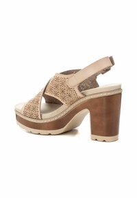 Sandalia de tacón beige con un patrón floral troquelado en cuero, plantilla acolchada y tacón cuadrado marrón. Correa ajustable en la parte trasera.