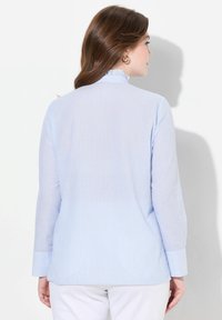 Pruhovaná svetle modrá blůza s dlouhými rukávy a límečkem, se volánkovým detailem na výstřihu a mírně zakřiveným lemem.