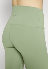 Zielone legginsy z wysokim stanem, bezszwowe, z małym logo Nike na pasku i gładkiego, elastycznego materiału.