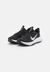 Zapatillas deportivas negras con parte superior de malla, acento del logotipo de Nike en blanco, suela texturizada y cordones planos. Diseño ligero y de perfil bajo.