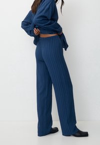 Marinblå, rutiga vida byxor och en matchande långärmad skjorta med avslappnad passform, tillverkade av mjukt, texturerat tyg. Svarta skor fulländar looken.