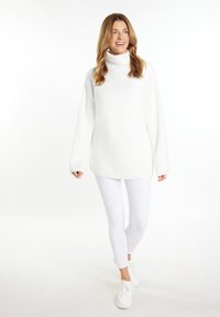Biały, oversized sweter z golfem o prążkowanej teksturze, w połączeniu z dopasowanymi białymi dżinsami i białymi sneakerami. Prosty i nowoczesny design.