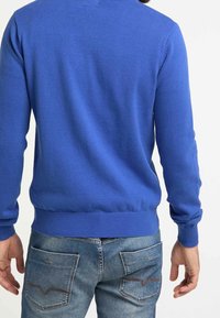 Kungsblå tröja med en figurnära design, stickad textur och ribbade ärmslut och nederkant. Matchad med ljusblå jeans med bakfickor.