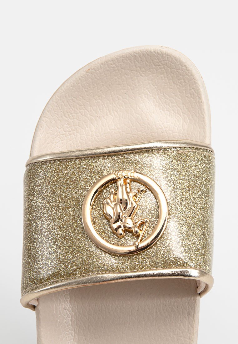 Goldschimmernde Rutsch-Sandale mit einem breiten Riemen, der ein rundes Emblem und glänzende Verzierungen aufweist. Strukturierte Sohle in hellbeige.