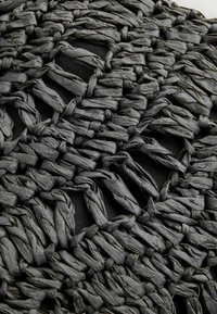 Schwarzer gewebter Teppich aus dickem Material mit einer strukturierten Oberfläche, die aus miteinander verbundenen Schlaufen und Öffnungen für ein organisches Muster besteht.