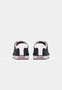 Czarne trampki z białymi akcentami, z płóciennym wierzchem, gumową podeszwą i czerwonym logo "HILFIGER" na pięcie. Klasyczny model na sznurówki.