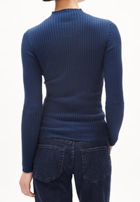 Pull bleu marine côtelé à manches longues et col montant, caractérisé par une coupe ajustée et une texture subtile. Associé à un jean denim foncé.