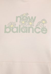 Lys rosa hettegenser med "new balance"-tekst i grønt og hvite tusenfryd som aksenter, glatt tekstur og avslappet design.