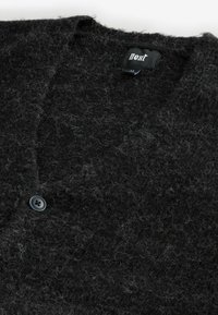 Schwarze Cardigan mit Struktur aus flauschigem Material. Hat einen tiefen V-Ausschnitt und einen einzigen dunklen Knopfverschluss. Etikett im Kragen sichtbar.
