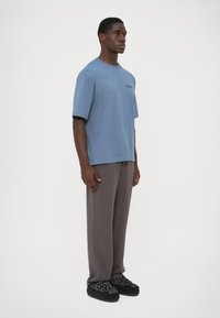 Pamučna plava majica s kratkim rukavima, okruglim izrezom i detaljem s logom. Uparena s sivim širokim hlačama i crnim cipelama s uzorkom.