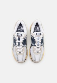 Nike Vomero 5 sneakers i vit, marinblå och beige nät med reflekterande detaljer och en texturerad gummiyttersula. Har snörning och varumärkeslogotyp.