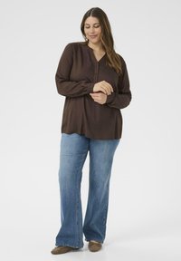 Brun långärmad skjorta med henley-krage och knappdetaljer, i kombination med blå utsvängda jeans. Slät tygkvalitet och avslappnad passform.