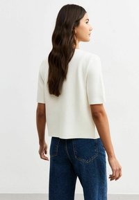 Top bianco a maniche corte con scollatura tonda e vestibilità morbida, abbinato a jeans in denim blu a vita alta con tasche posteriori.
