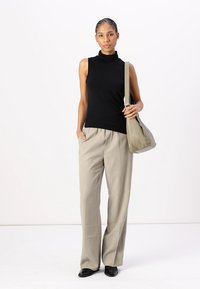 Haut noir sans manches à col roulé, pantalon large beige et sac à bandoulière gris. La tenue présente des textures lisses et une palette de couleurs neutres.