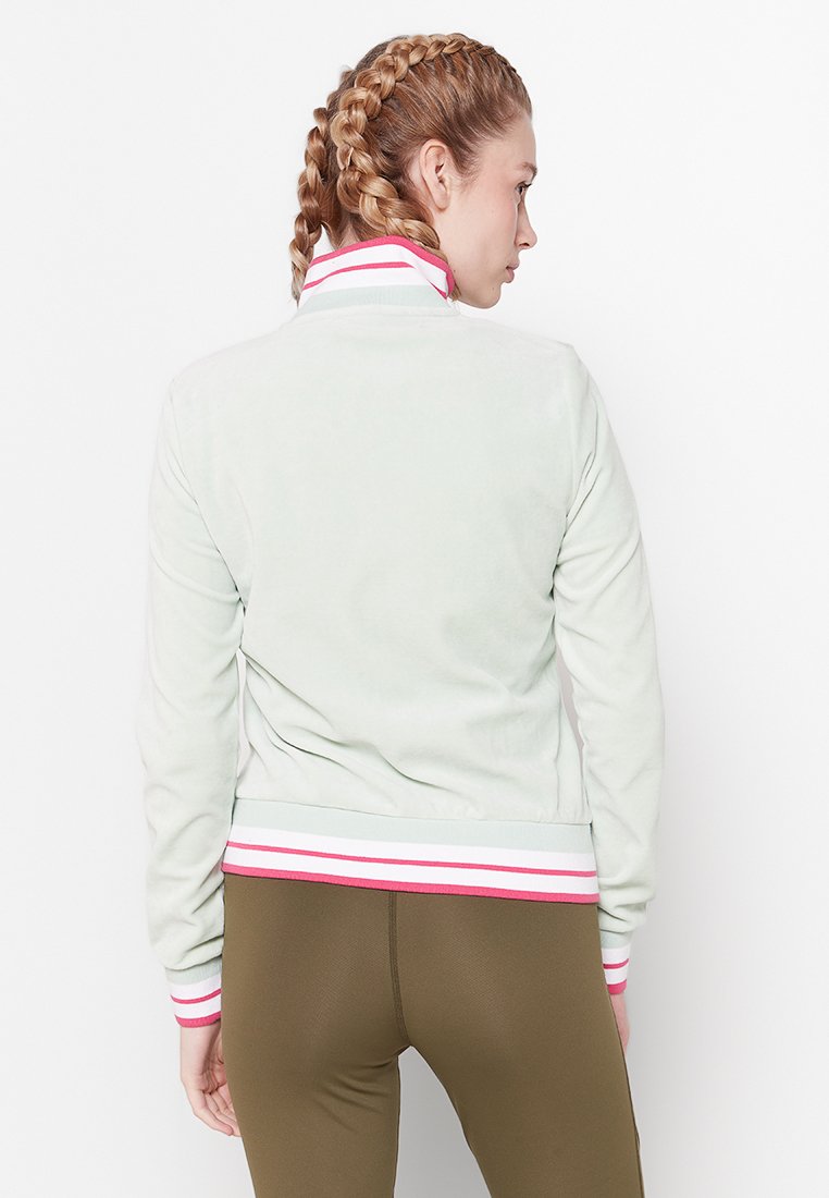 Giacca in velluto verde chiaro con collo alto e orlo a coste a righe rosa e bianche. Texture liscia, maniche lunghe e design attillato.