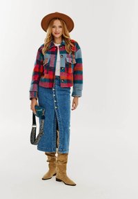 Farebný károvaný kabát v odtieňoch červenej, modrej a oranžovej, doplnený džínsovou sukňou s predným radom gombíkov. Hnedé voľné čižmy dokončujú vzhľad.