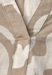 Gros plan d'un tissu beige et blanc cassé à motifs avec des coutures visibles le long d'une couture et des plis qui se chevauchent.