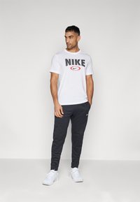 Hvit Nike t-skjorte med svart logo, paret med mørkegrå joggebukser og hvite sportsko, som viser en avslappet, sporty stil.