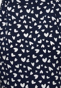 Donkerblauwe stof met een herhalend patroon van witte harten in verschillende formaten. Gladde textuur; materiaal lijkt licht en ademend te zijn.