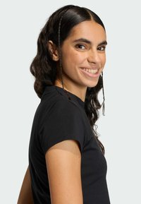 Čierne tričko s krátkym rukávom a priliehavým strihom. Modelka ukazuje bočný pohľad, na ktorom sa nachádza hladká látka a oblé výstrih.