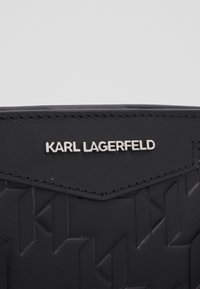 Czarny skórzany portfel z teksturowanym geometrycznym wzorem. Srebrne logo "KARL LAGERFELD" wytłoczone na froncie. Czyste detale szwów.