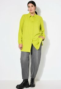 Limoengroene, lange mouwen shirt met een gestreept patroon, knoopsluiting aan de voorkant, twee borstzakken en een losse pasvorm, gecombineerd met grijze slouchy broeken en zwarte laarzen.