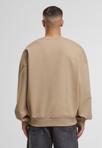 Beige oversized sweatshirt med sænket skuldre, ribstrikkede manchetter og kant. Blød tekstur, minimalistisk design uden mønstre.