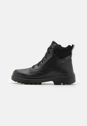 Botín de cuero negro con un cuello de ante texturizado, diseño con cordones, suela de goma con patrones de agarre y etiqueta GORE-TEX impermeable.