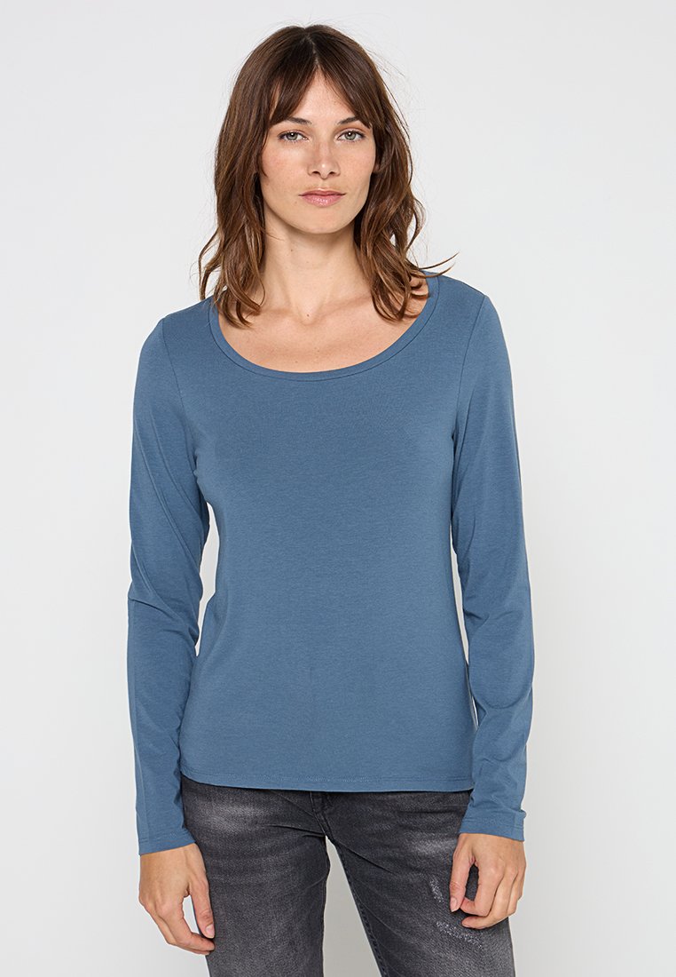 Langarmtop in gedempt blauw, gemaakt van zachte katoen. Heeft een brede ronde hals en een getailleerde pasvorm. Gestyled met donkergrijze denim.