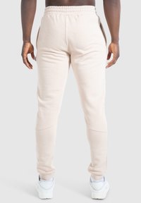 Beige Sweatpants mit einem elastischen Bund und Seitentaschen. Glatte Textur mit schmal zulaufenden Beinen und gerippten Bündchen. Kombiniert mit weißen Turnschuhen.