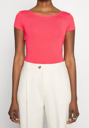 Heldere koraalkleurige aansluitende T-shirt met korte mouwen en een ronde halslijn, gecombineerd met beige hoge taillebroeken met een knoopsluiting aan de voorkant.